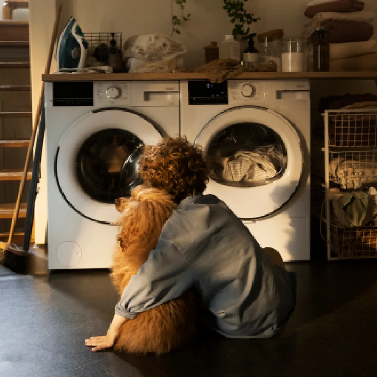 Barn med hund sitter framför tvättmaskin och torktumlare